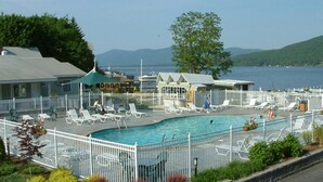Un espace piscine doté de chaises longues blanches et d’une terrasse délimitée par une clôture, offrant une vue sur une étendue d’eau avec des collines en arrière-plan.