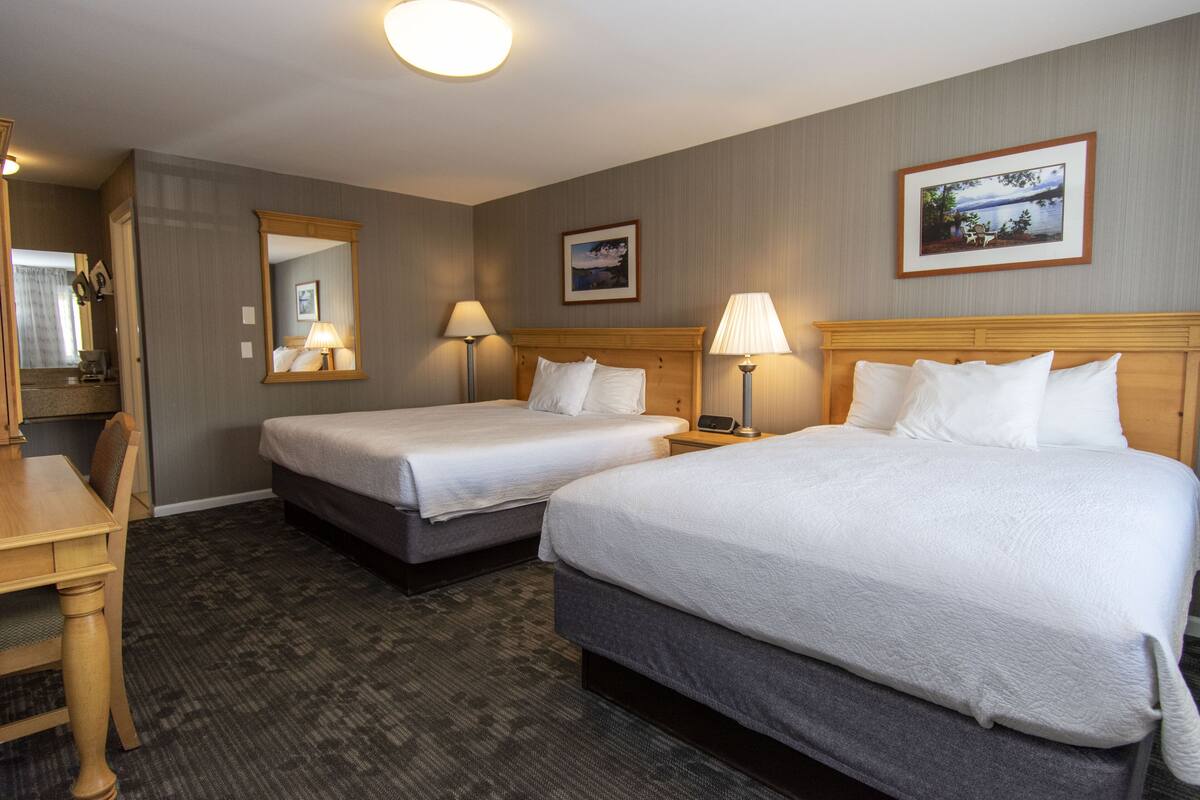 A hotel room with two beds, a desk, and a mirror.
