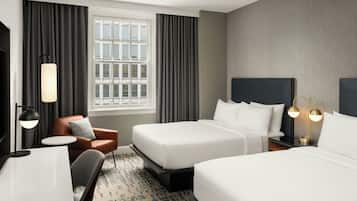 A hotel room with two beds, a desk, a chair, a window with curtains, and a lamp.