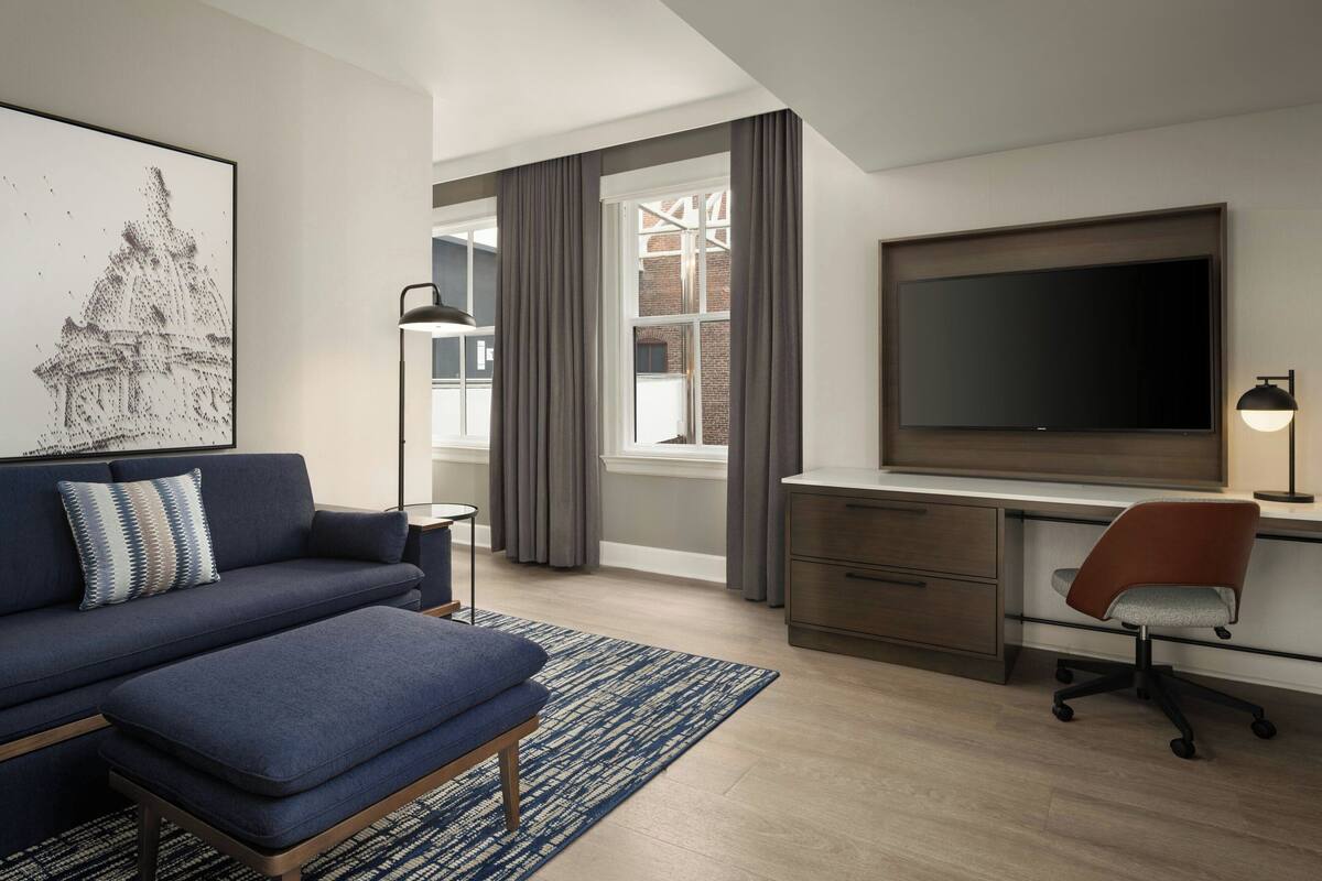 A modern hotel room with a large flat-screen TV, a sofa, a desk, and a chair.