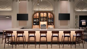 A bar area with a long counter, multiple stools, and a display of bottles. - Courtyard by Marriott Philadelphia Downtown (Philadelphia)