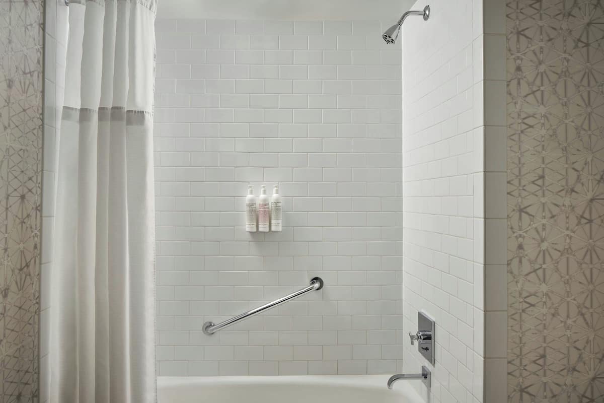 A modern bathroom with white tiled walls, a shower curtain, a grab bar, and toiletries on the wall.