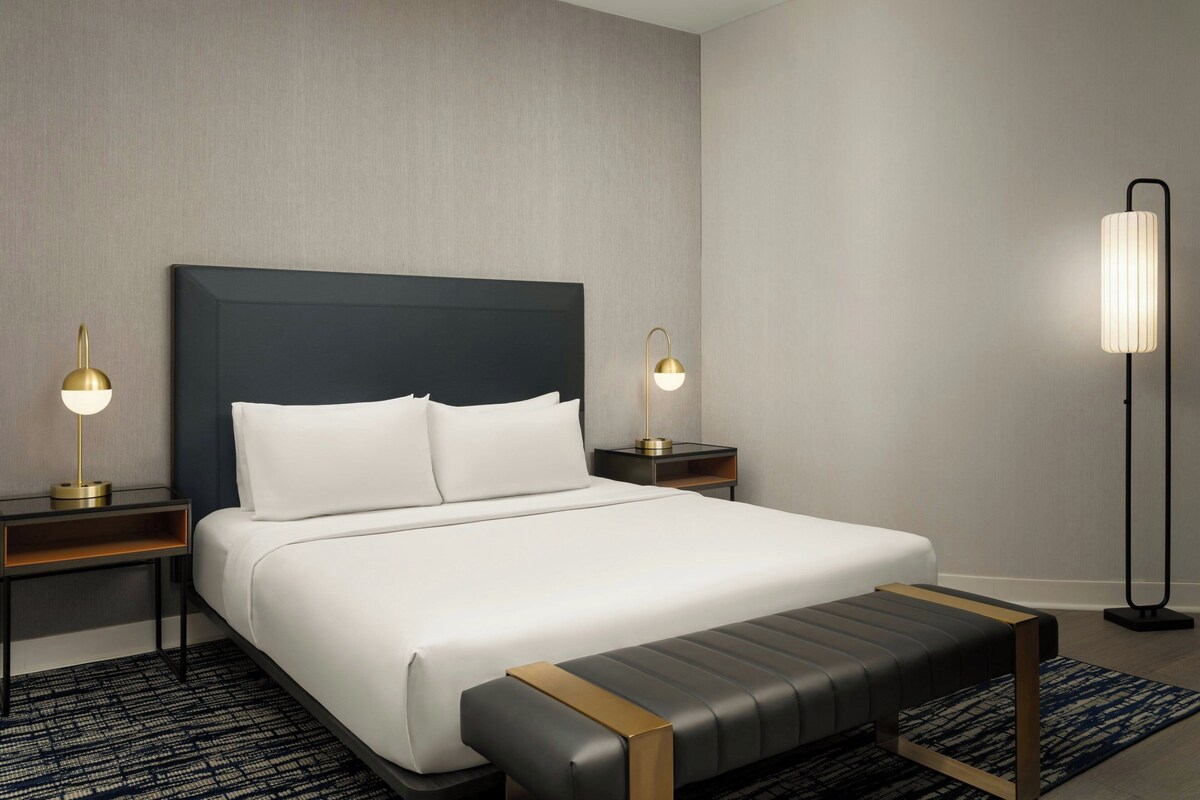 A hotel room with a large bed, two bedside tables with lamps, a bench, and a floor lamp.