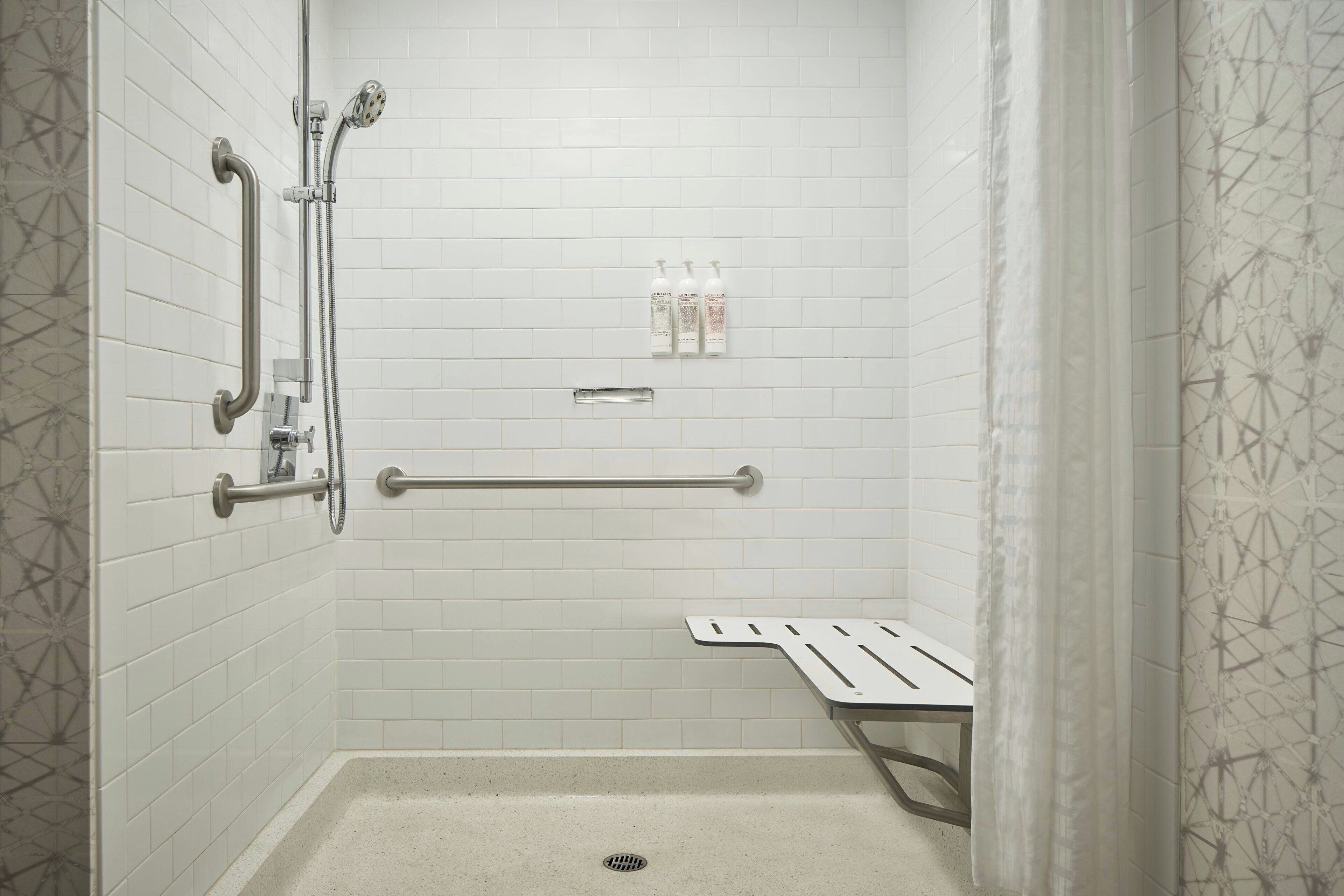 A shower with a grab bar, a bench, and a shelf with toiletries.