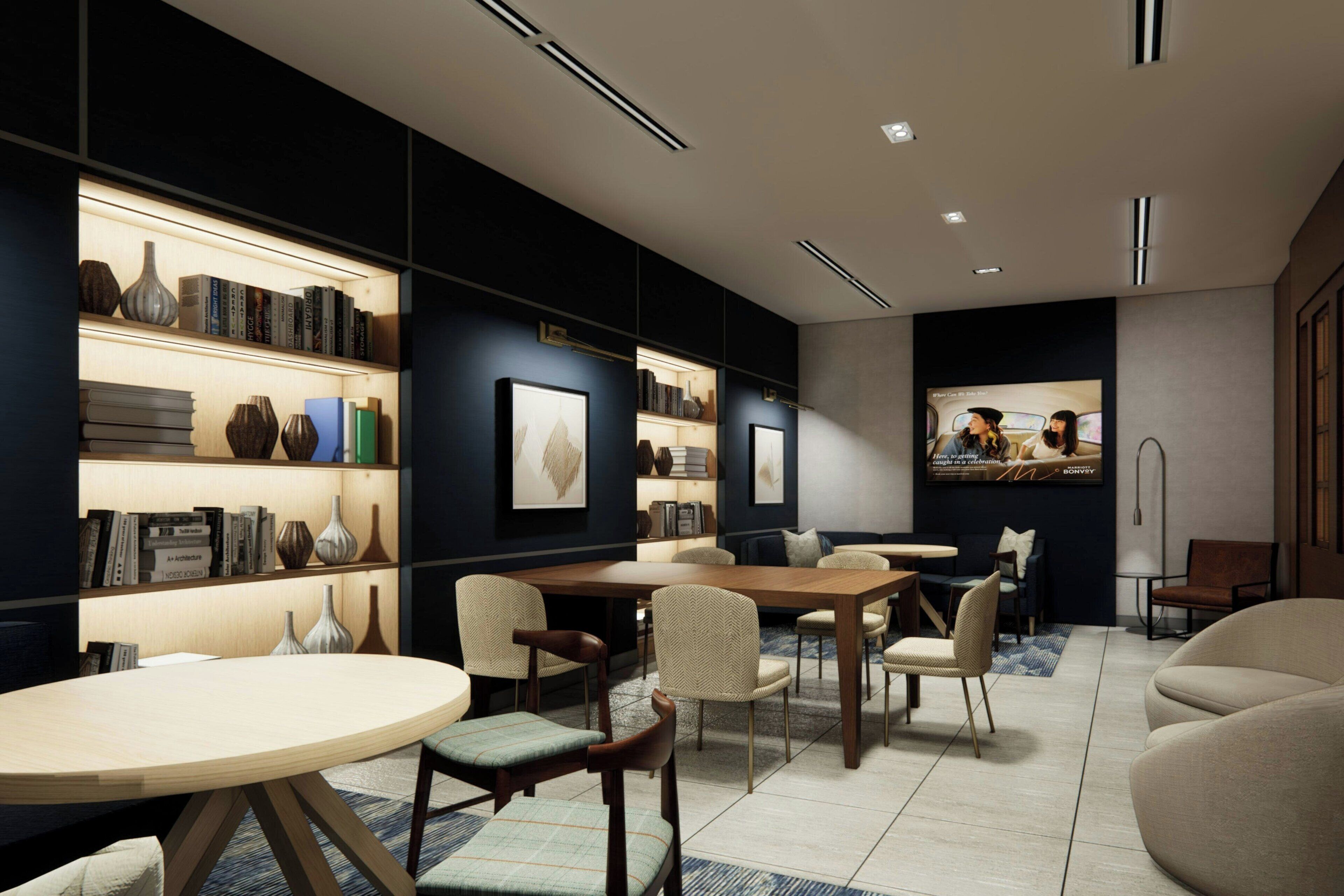 A modern library with bookshelves, a round table, and comfortable seating.