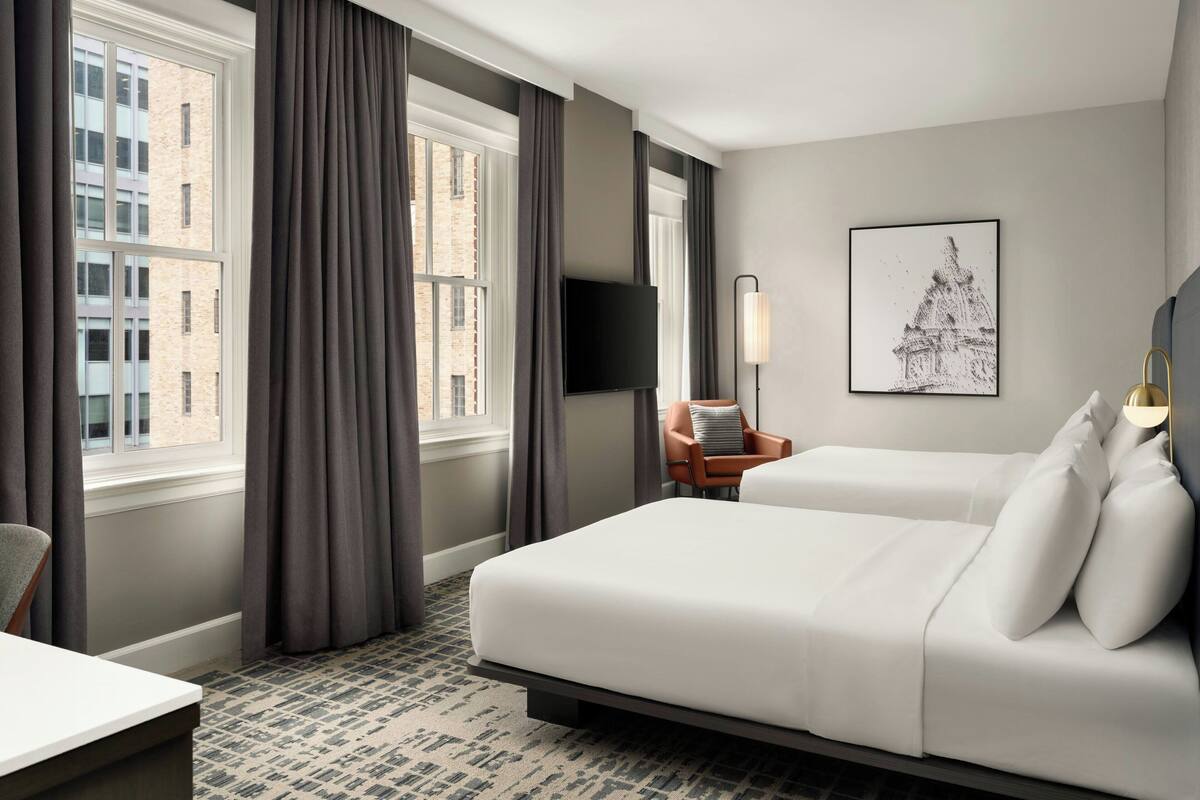 A hotel room with a large bed, a desk, a chair, a TV, and a window with curtains.