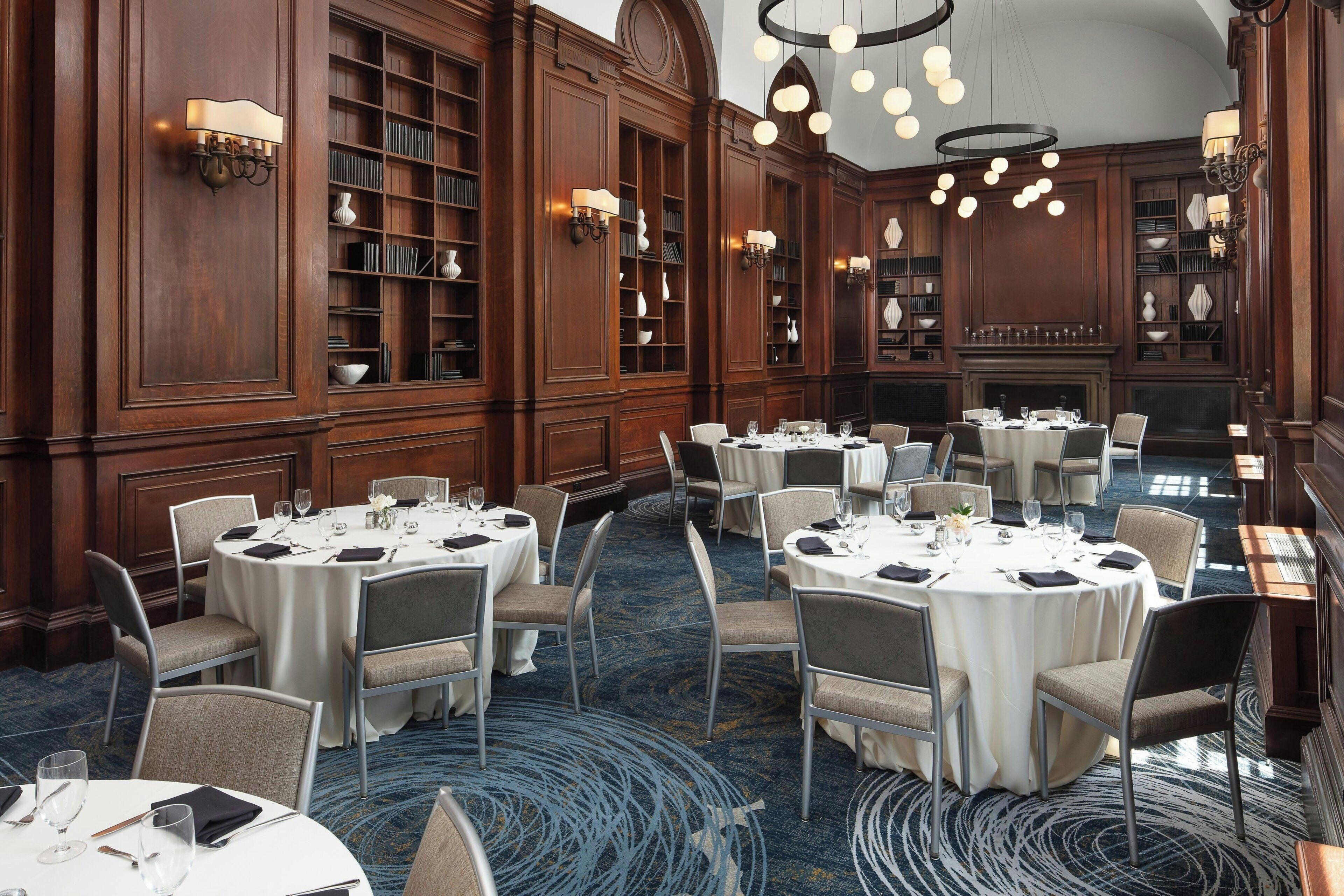A formal dining room with round tables, chairs, and a fireplace.