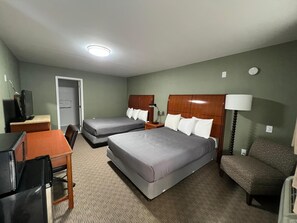 Ett hotellrum med två sängar, ett skrivbord, en stol, en TV och en lampa.