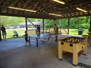 Ett utomhusområde med tak, där det finns ett bord för bordtennis, ett fotbollsspel och ett picknickbord.
