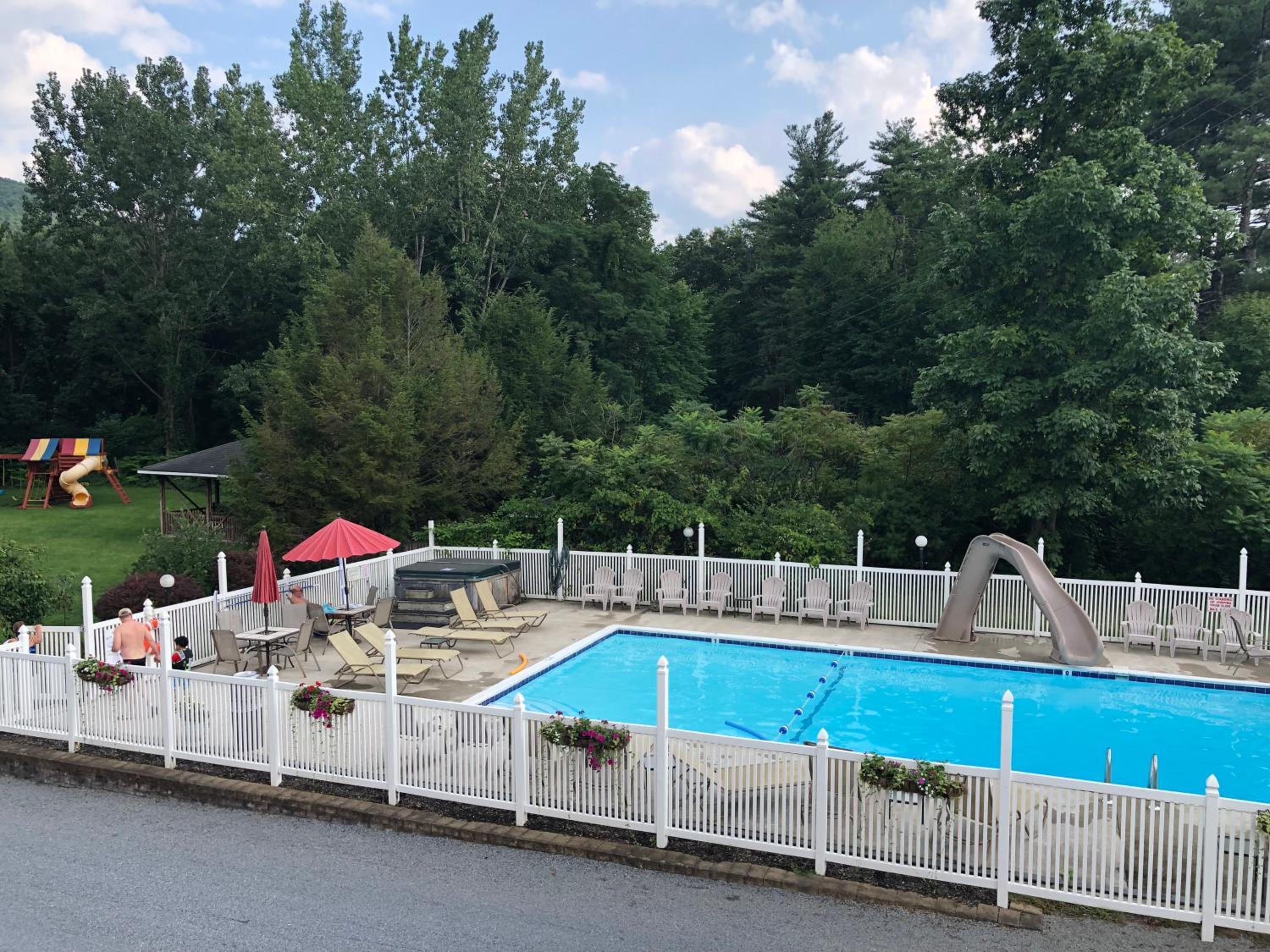 A swimming pool with a white fence, lounge chairs, and a slide in the background.