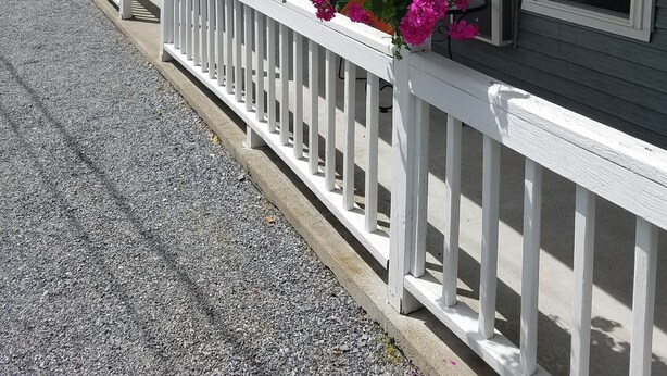 A row of white-framed buildings with a gravel driveway and a white railing. - Lyn Aire Motel (Lake George)