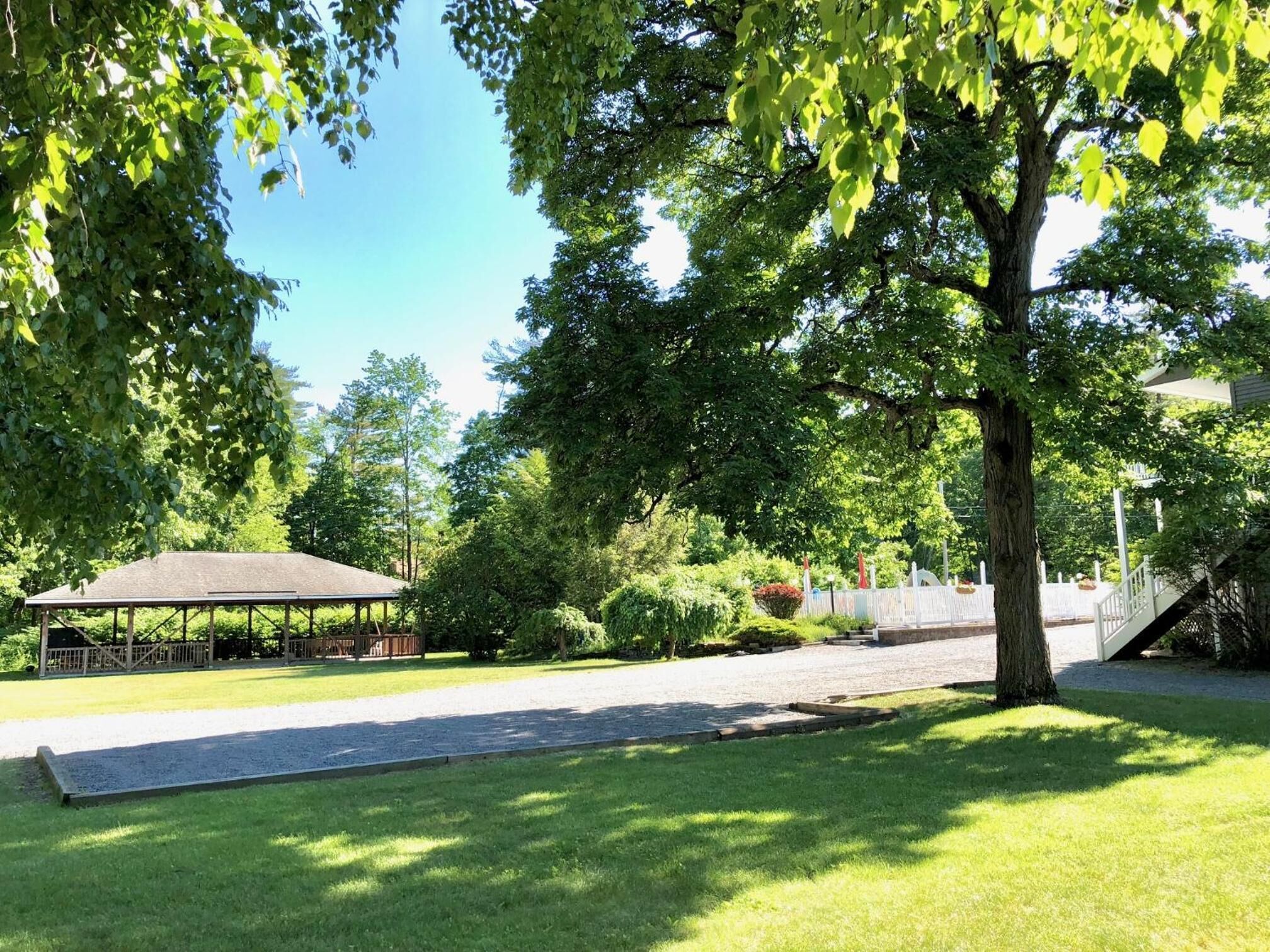 A covered outdoor area with a gravel path, surrounded by lush greenery and trees.