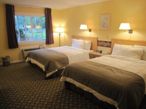 Une chambre d’hôtel avec deux lits, une fenêtre avec des rideaux, un radiateur, une poubelle et deux lampes fixées au mur.
