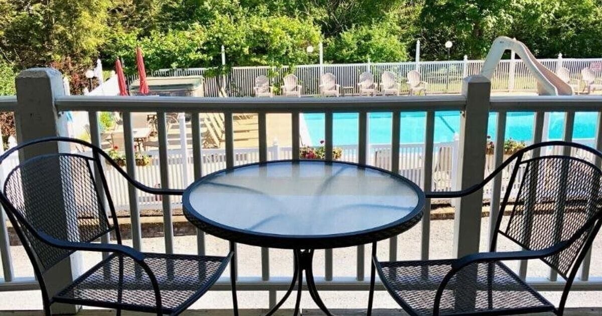 A poolside area with a round table and two chairs, a white fence, and a slide in the background.