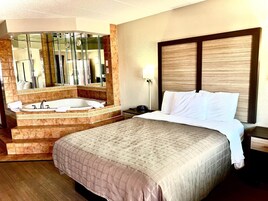Una habitación de hotel con una cama grande, un baño separado con bañera y un espejo amplio.