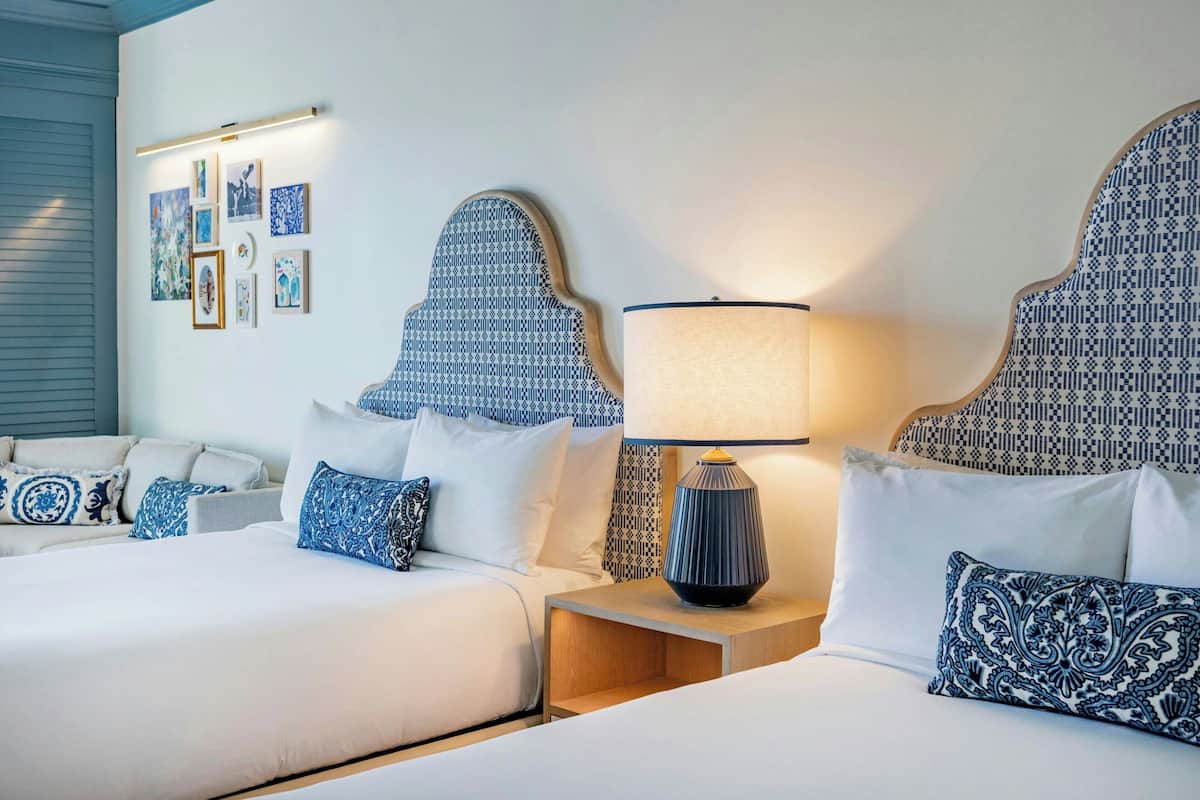 Ein Hotelzimmer mit zwei Betten, einem Nachttisch mit Lampe und einer Wand mit gerahmten Kunstwerken.