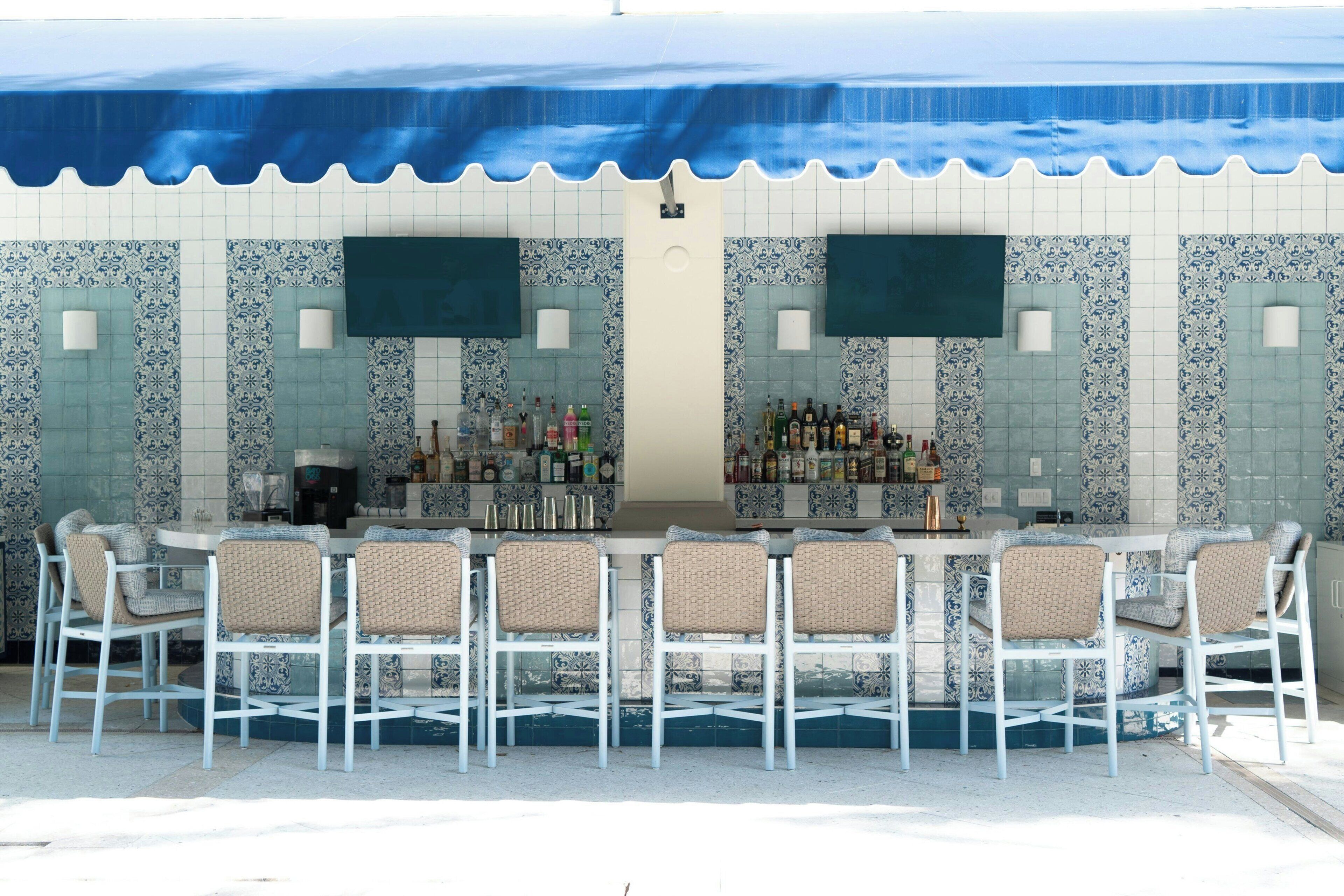 Un espace bar avec un mur recouvert de carreaux, des tabourets de bar blancs et une variété de bouteilles.