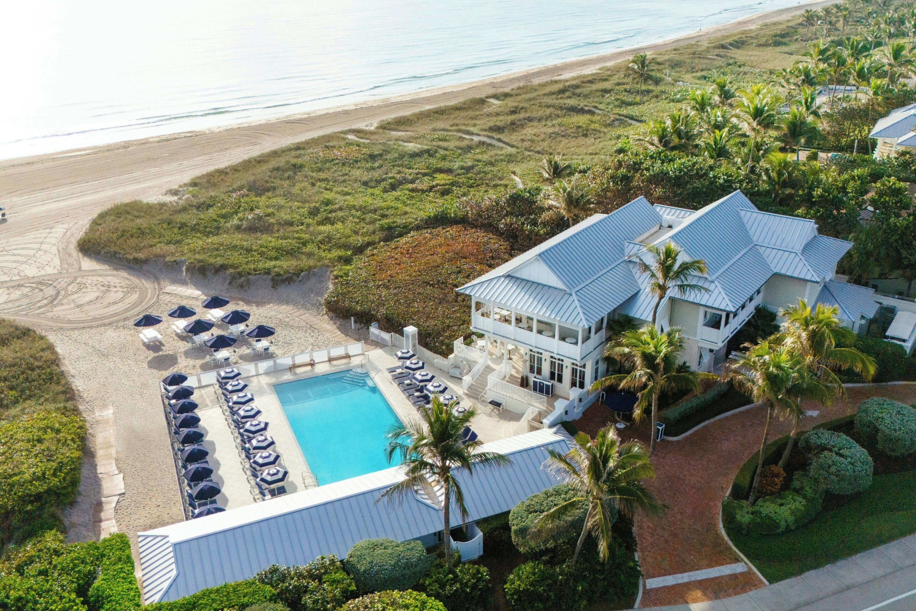 An aerial view of a resort with a pool, beach, and palm trees.