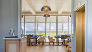 A spacious room with a large window, a ceiling light fixture, and a seating area with tables and chairs. - The Seagate Hotel, Golf & Beach Club, Autograph Collection (Delray Beach)