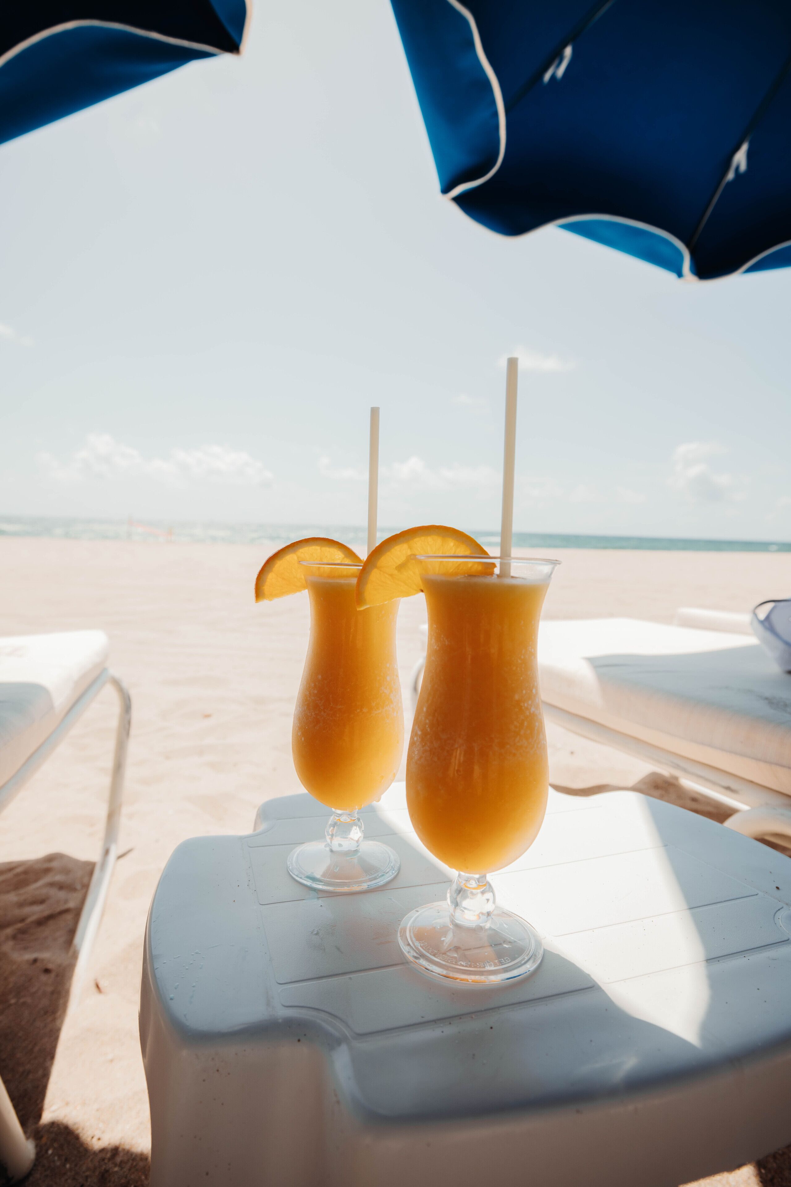 Two drinks on a white table with a beach view in the background.