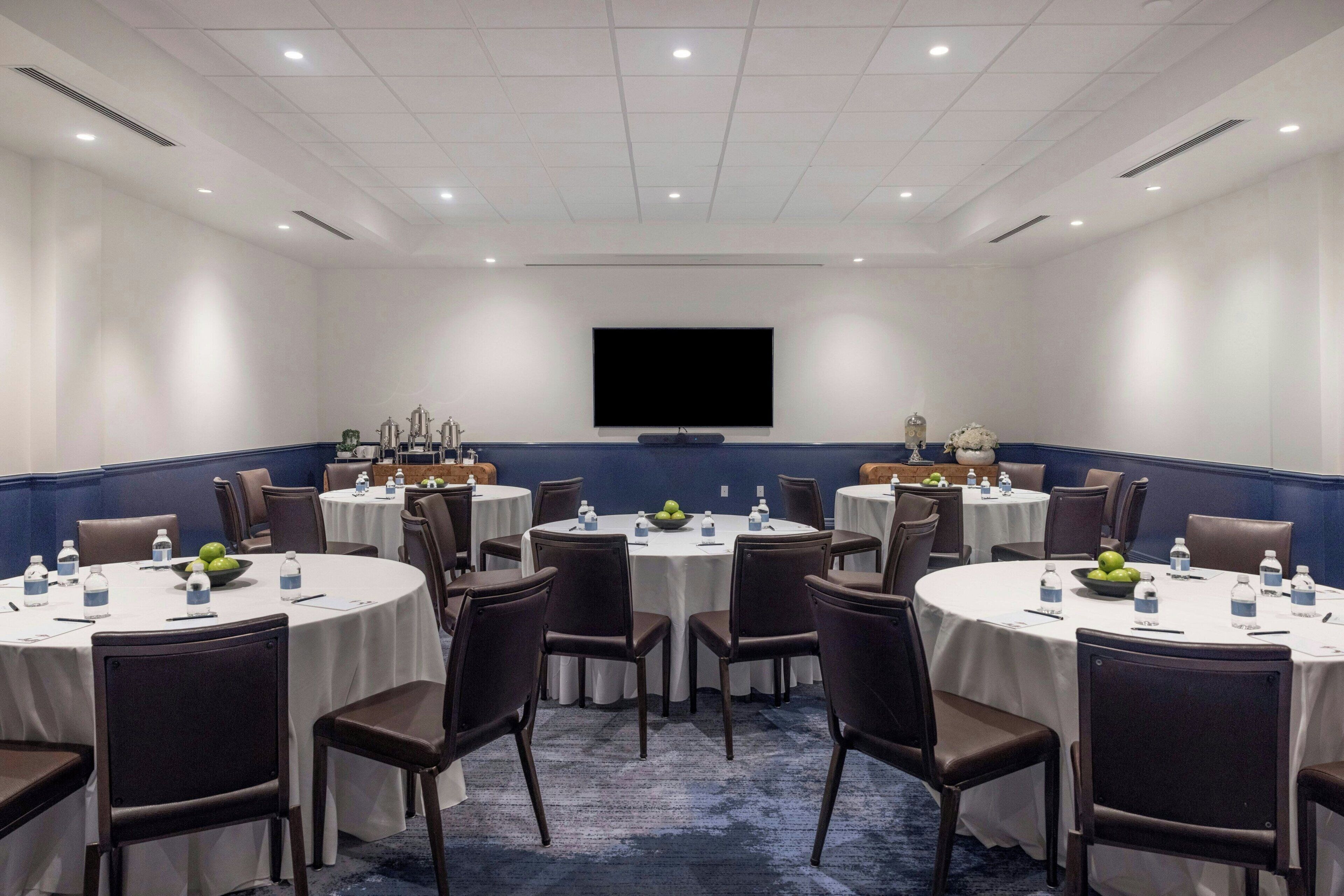 A conference room with round tables, chairs, and a large screen.