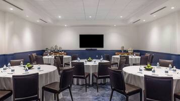 A conference room with round tables, chairs, and a large screen.