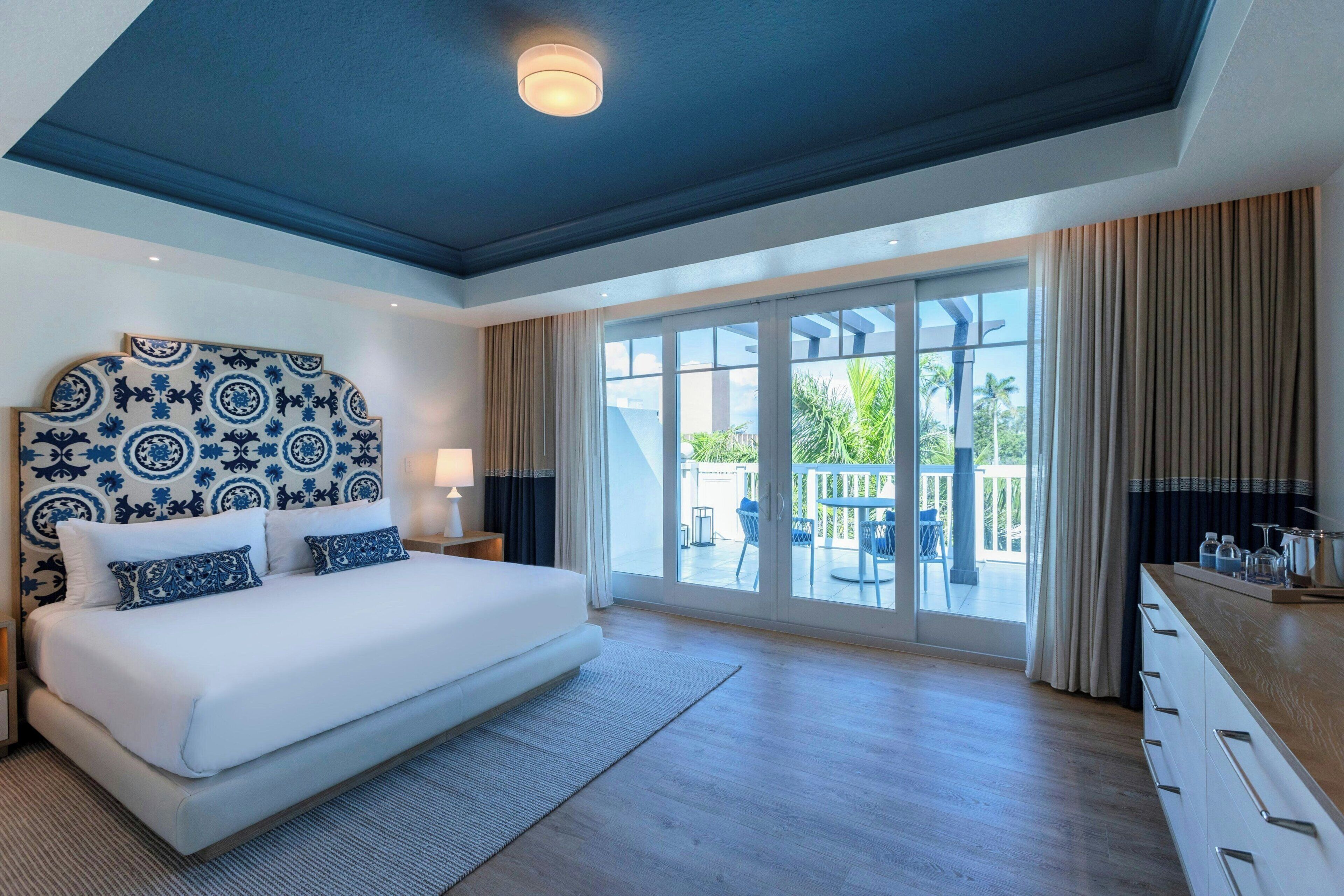 Un dormitorio amplio con una cama grande, un cabecero con diseño, vistas al balcón exterior y un diseño de techo moderno.
