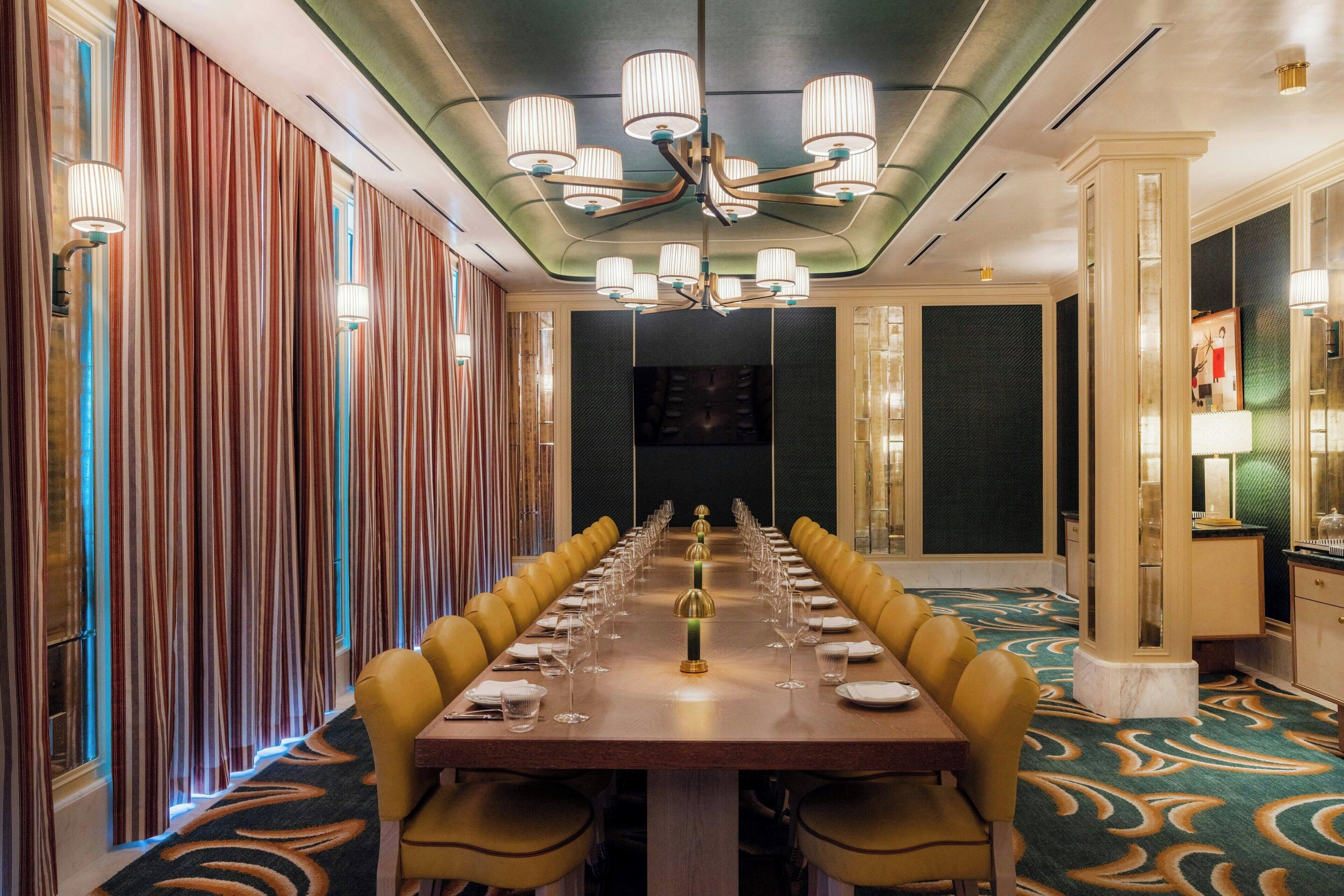 A long dining table with chairs, a chandelier, and a patterned carpet.