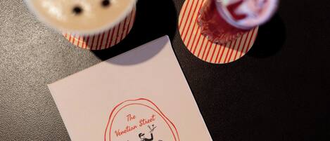 A menu from The Venetian Street Hotel Bar, featuring a drink with a straw and a dessert with a cherry on top.