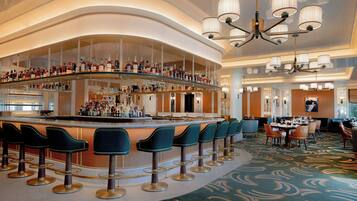 Eine Bar mit mehreren Hockern und einer gebogenen Bar, umgeben von einem gemusterten Teppich und Kronleuchtern.