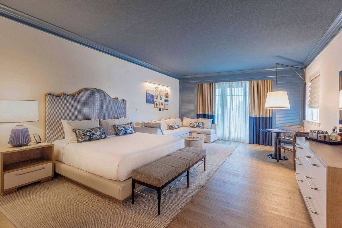 Ein modernes Hotelzimmer mit einem großen Bett, einer Couch, einem kleinen Tisch und einem Schreibtisch mit Schubladen.