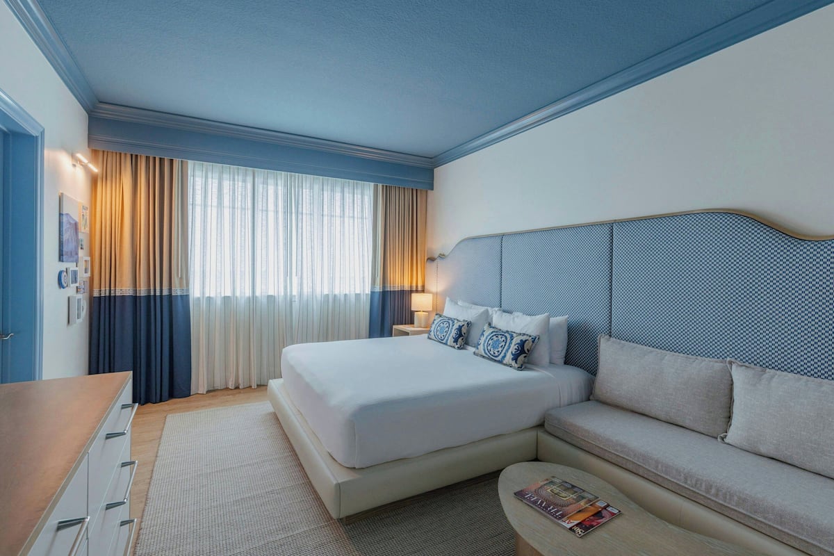 Ein Hotelzimmer mit einem großen Bett, einer Couch, einem Schreibtisch und einem Fenster mit Vorhängen.