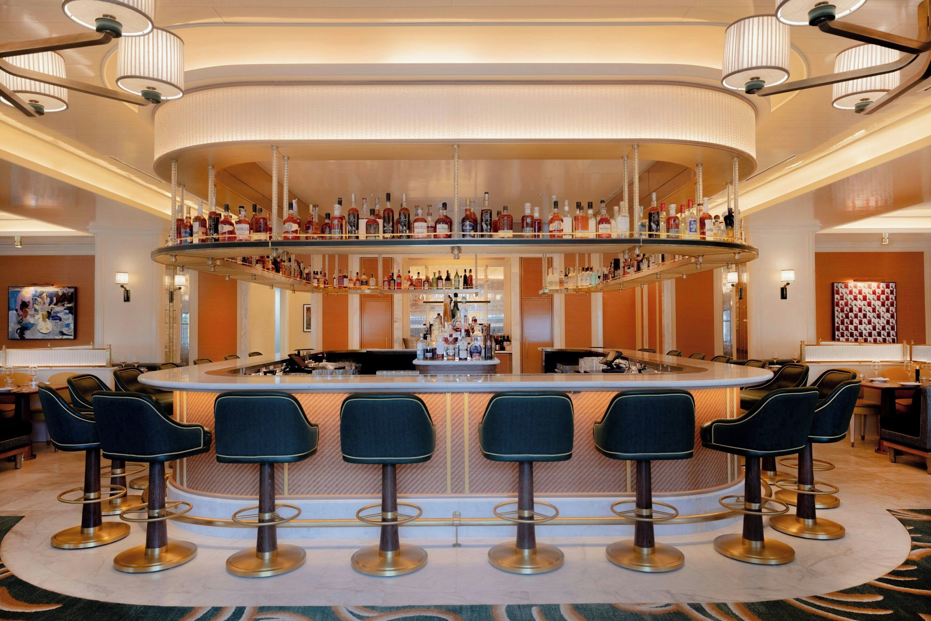 Eine Bar mit mehreren Hockstühlen, einer Theke in der Mitte und einer Auswahl an Flaschen.