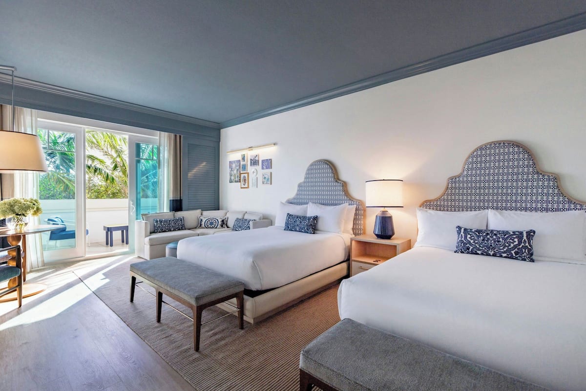Ein Hotelzimmer mit zwei Betten, einem Schlafsofa, einem kleinen Tisch und Blick ins Freie.