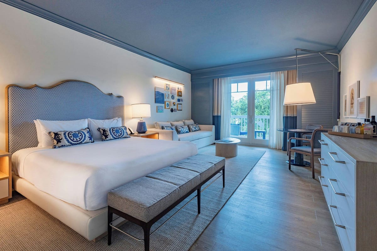 Ein modernes Hotelzimmer mit einem großen Bett, einer Sitzbank, einem Sofa, einem Essbereich und Blick ins Freie.