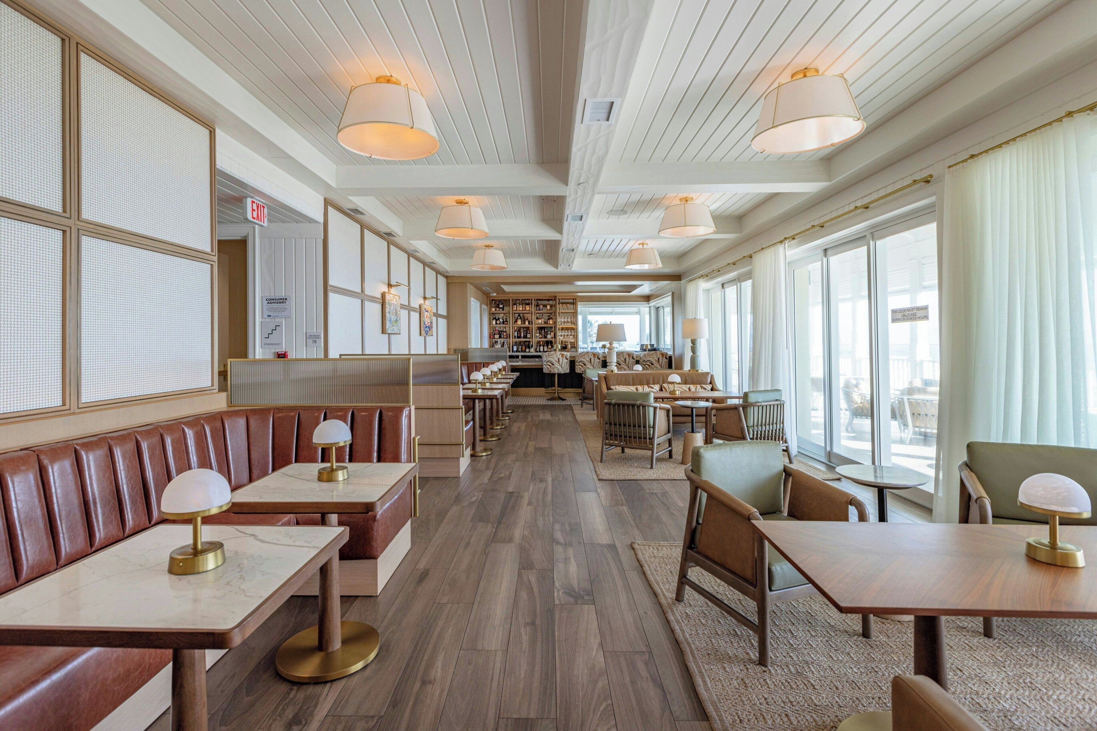 A spacious restaurant with wooden floors, leather booths, and tables with lamps.