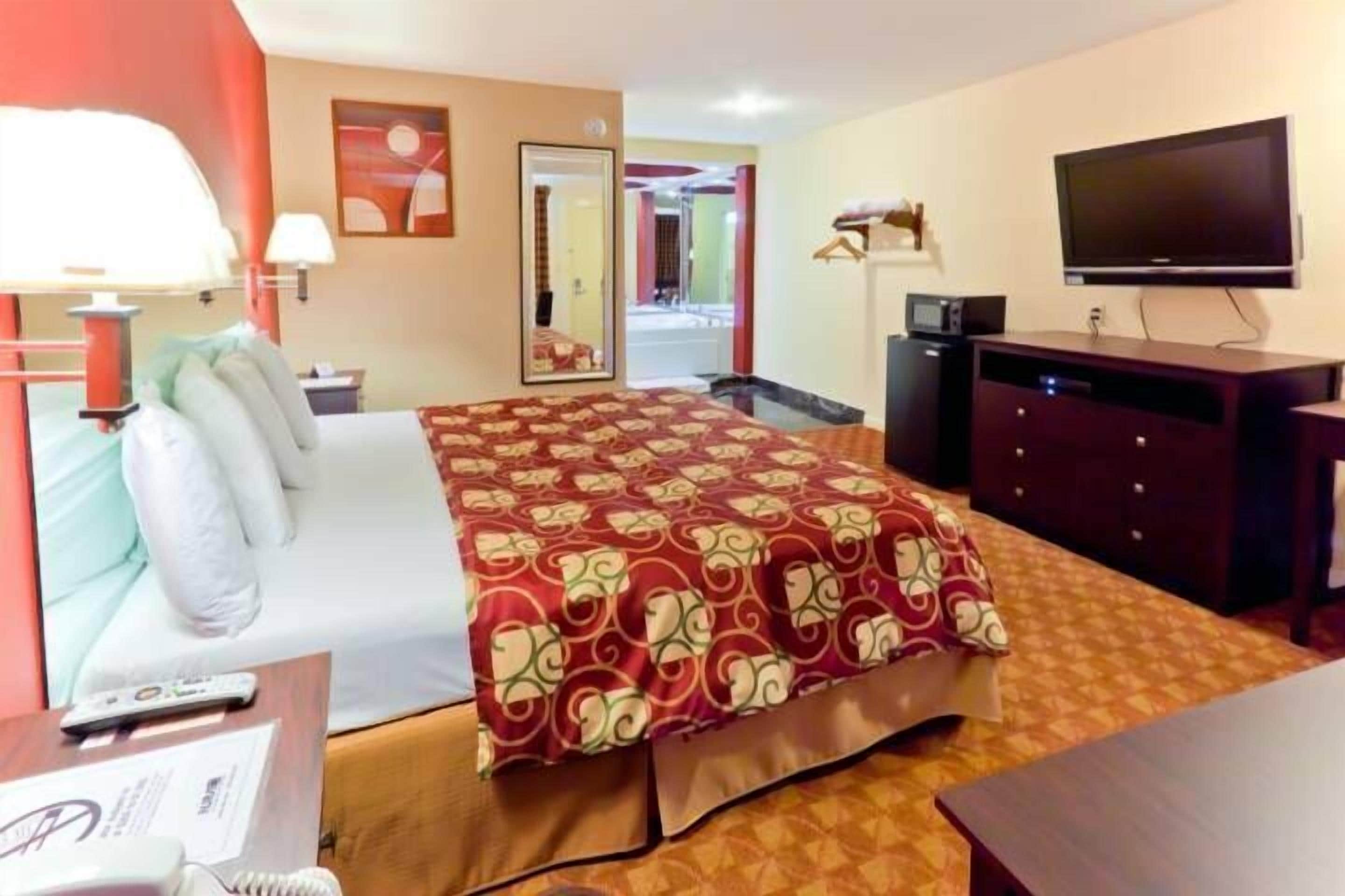 Habitación de hotel con cama, escritorio, teléfono, televisión y espejo.