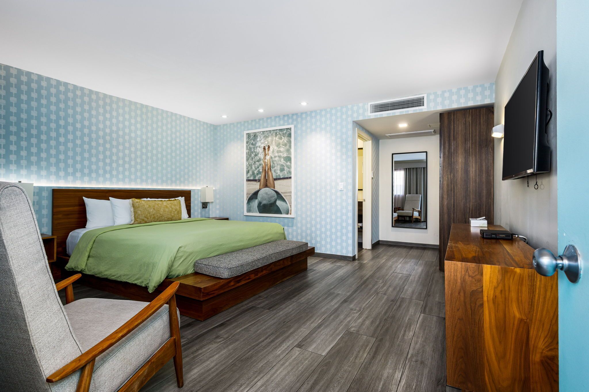 A modern hotel room with a bed, a wooden desk, a chair, and a television.