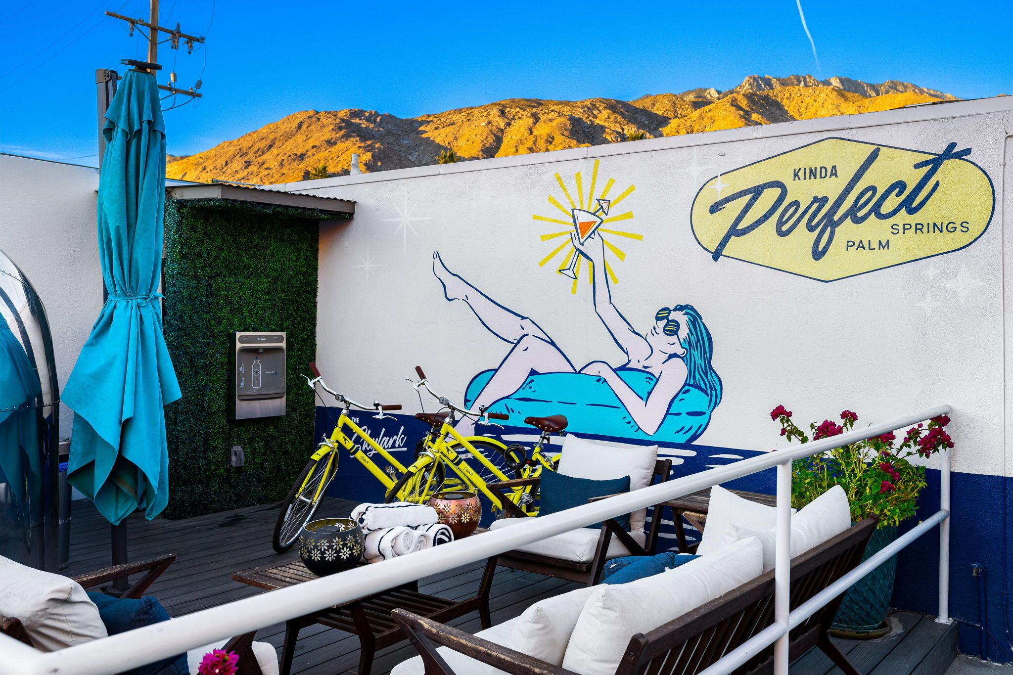 A deck with a mural of a woman relaxing, a yellow bicycle, and a sign reading "Kinda Perfect Springs Palm".