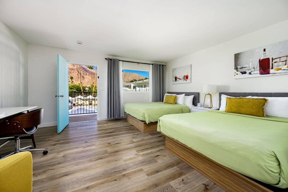 Quarto de hotel com duas camas, uma escrivaninha e vista para uma montanha e piscina.