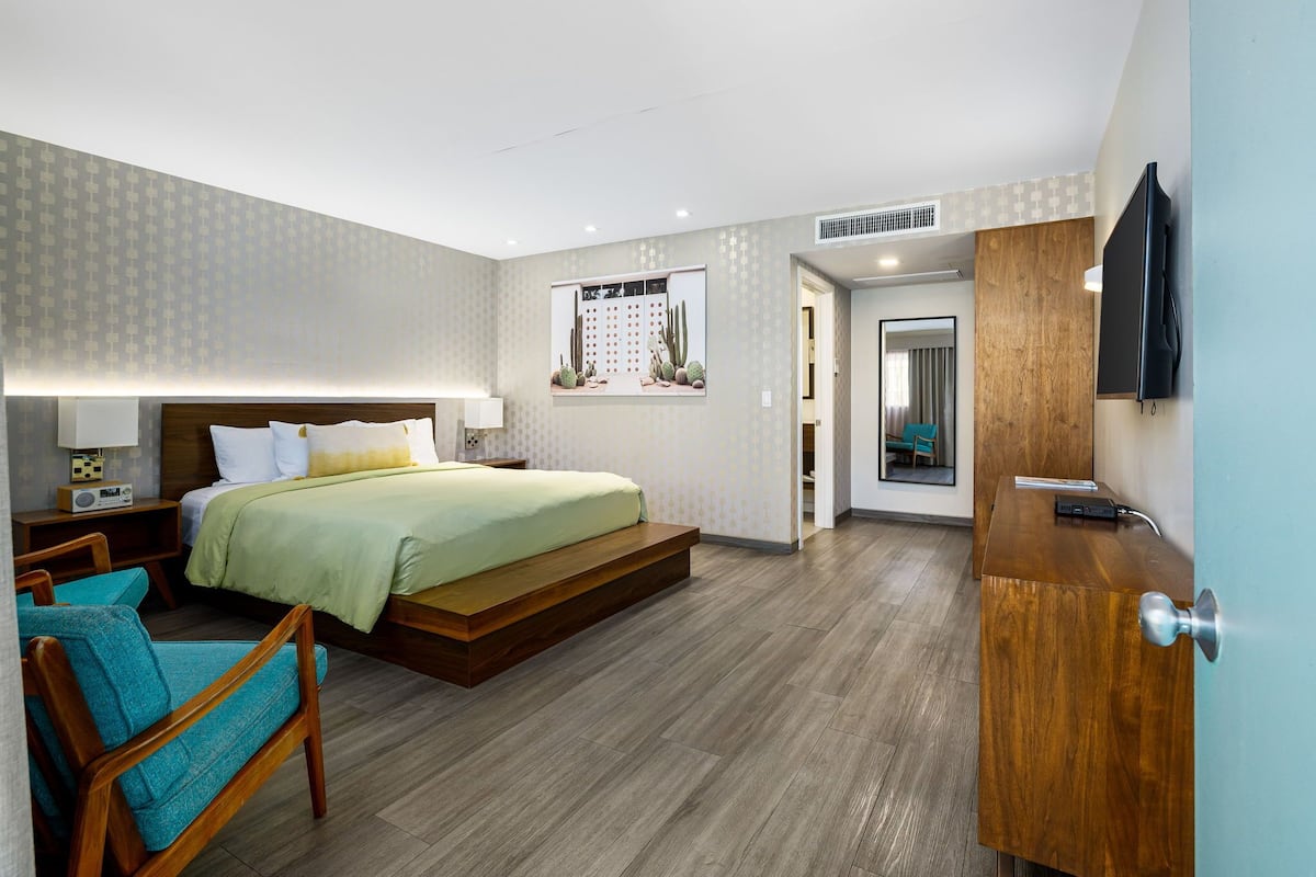 Quarto de hotel moderno com cama, escrivaninha, cadeira e televisão.