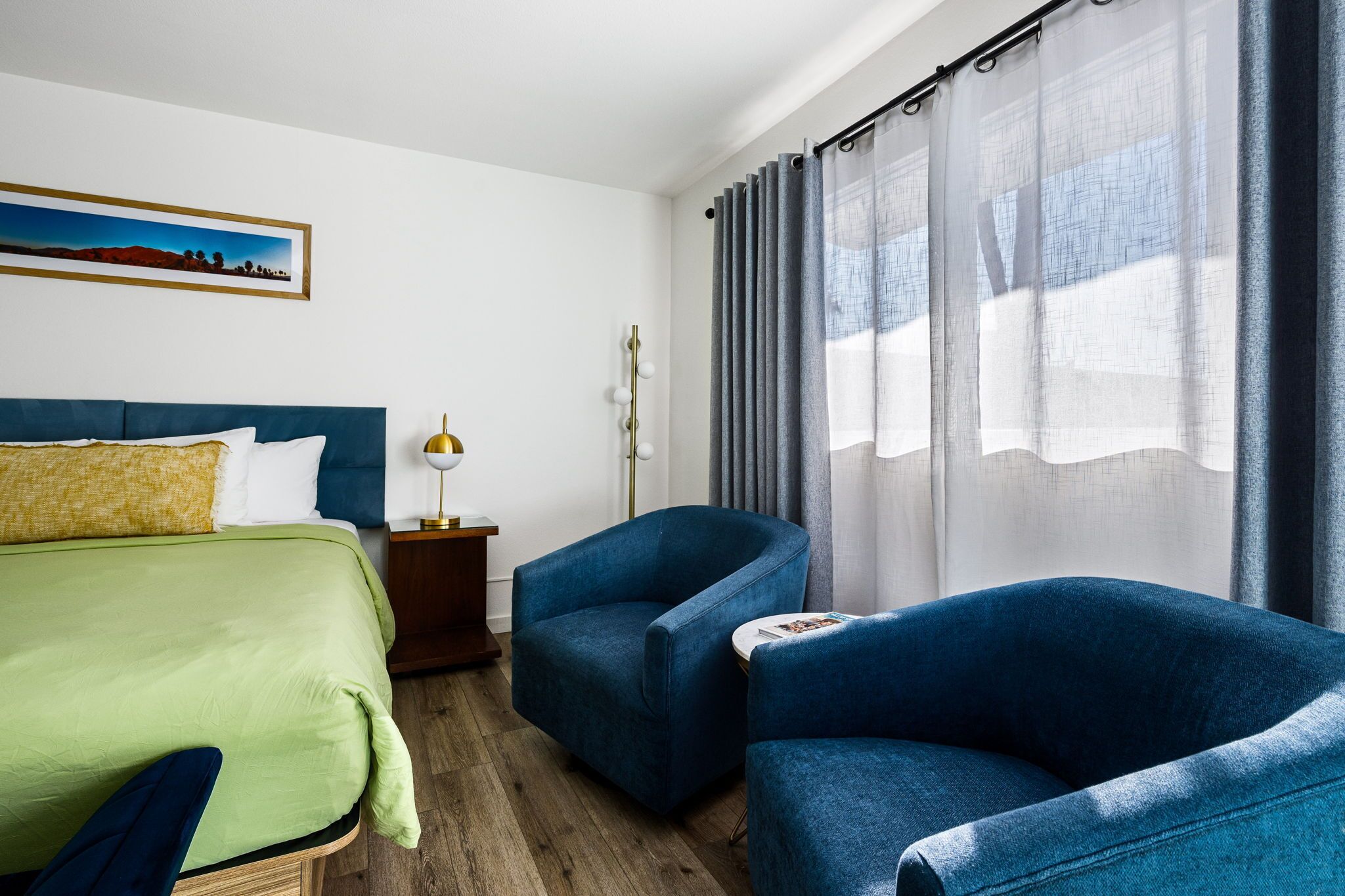 A hotel room with a bed, two armchairs, a nightstand, a lamp, and a window with curtains.