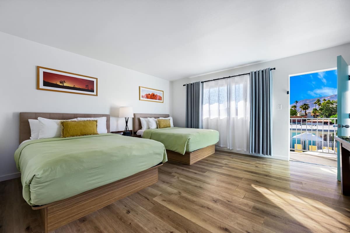 Quarto de hotel com duas camas, uma janela grande com cortinas, vista para uma piscina e palmeiras, e obras de arte nas paredes.