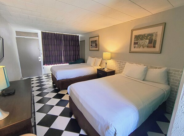 A hotel room with two beds, checkered floor, a desk with a lamp, and a door leading to another room. - Monaco Motel - Wildwood Beach & Boardwalk (Wildwood)