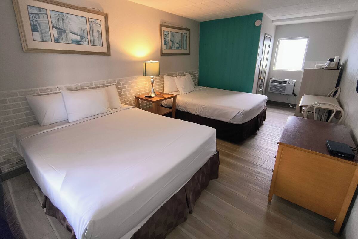 Ein Hotelzimmer mit zwei Betten, einem Schreibtisch, einer Lampe und Bildern an den Wänden.