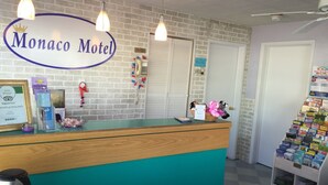 A reception desk at the Monaco Motel with a brick wall backdrop, a framed certificate, and a display of toiletries. - Monaco Motel - Wildwood Beach & Boardwalk (Wildwood)