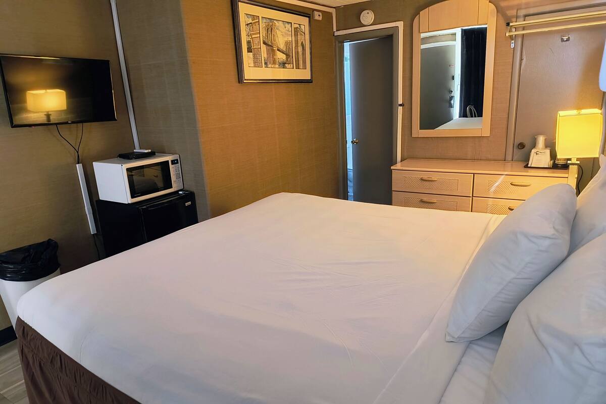 Ein Hotelzimmer mit Bett, Fernseher, Mikrowelle, Kommode und Spiegel.