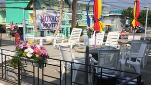 A sunny outdoor seating area with white plastic chairs and tables, a 'Monaco Motel' sign, and a stop sign. - Monaco Motel - Wildwood Beach & Boardwalk (Wildwood)