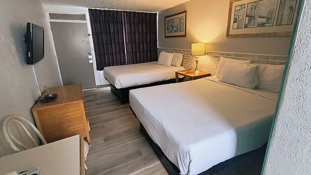 A hotel room with two beds, a desk, a chair, a TV, and artwork on the wall. - Monaco Motel - Wildwood Beach & Boardwalk (Wildwood)