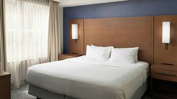 A hotel room with a large bed, a nightstand, a lamp, and a window with curtains.